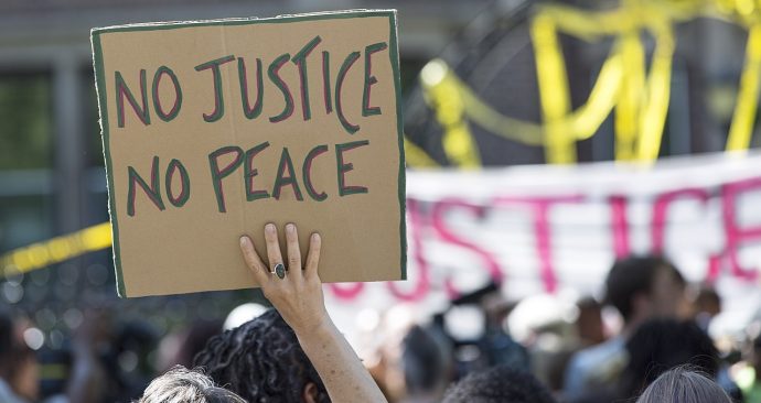 A_demonstrator_holds_a_No_Justice_No_Peace_sign_at_the_rally_for_Philando_Castile_outside_the_Governor’s_residence_in_St_Paul_MN_7-7-2016_(28137456646)